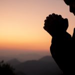 Silhouette of girl praying over beautiful sky background. Christ